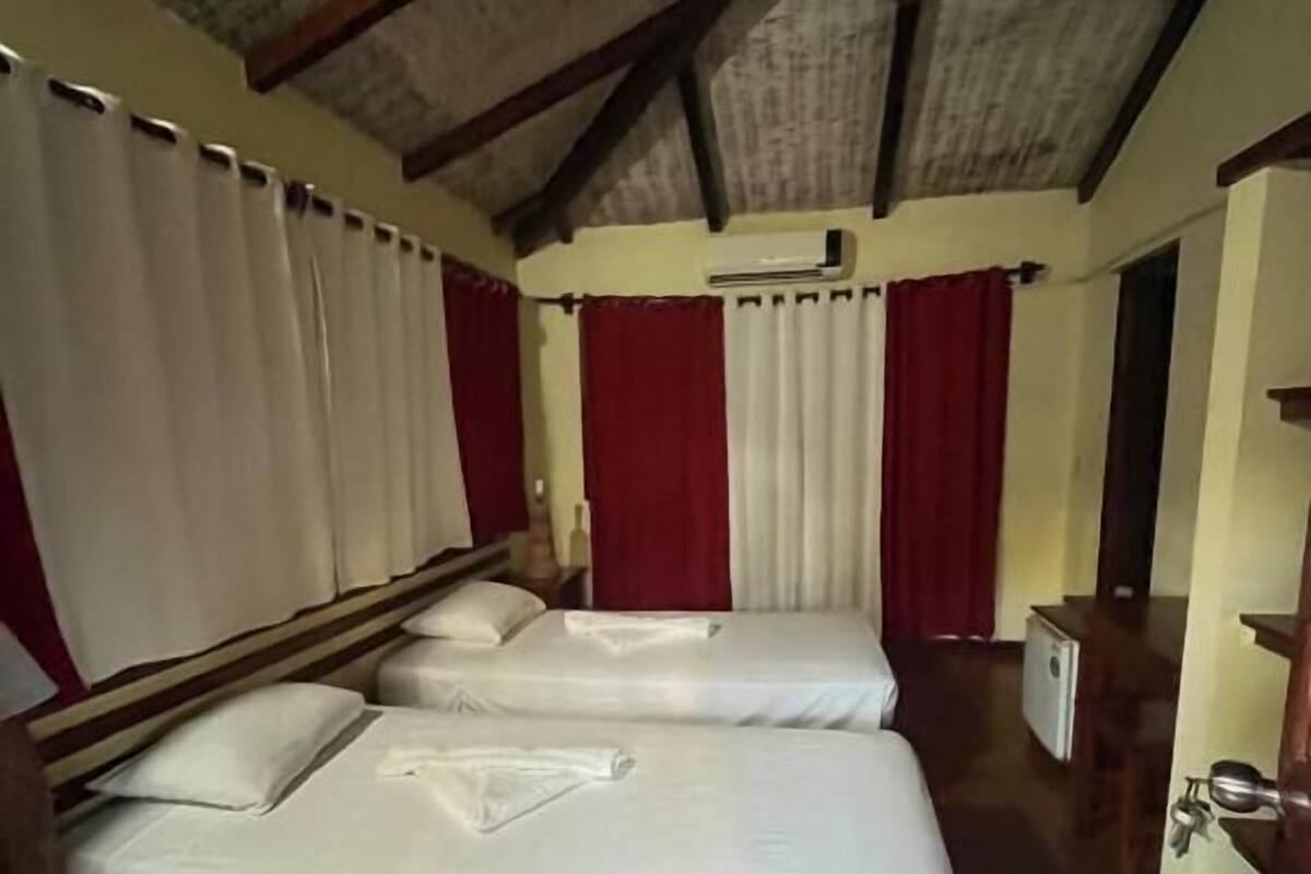 Una habitación con dos camas, techo de madera y un pequeño armario blanco.