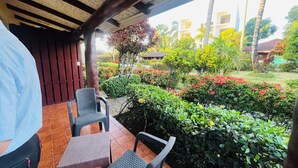 A covered outdoor seating area with two chairs and a table, surrounded by lush greenery and a view of buildings in the background. - hotel palococo (Las Terrenas)