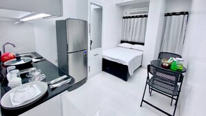 Une chambre d’hôtel compacte comprenant un coin cuisine, un lit, une petite table avec une chaise et un ventilateur de plafond.