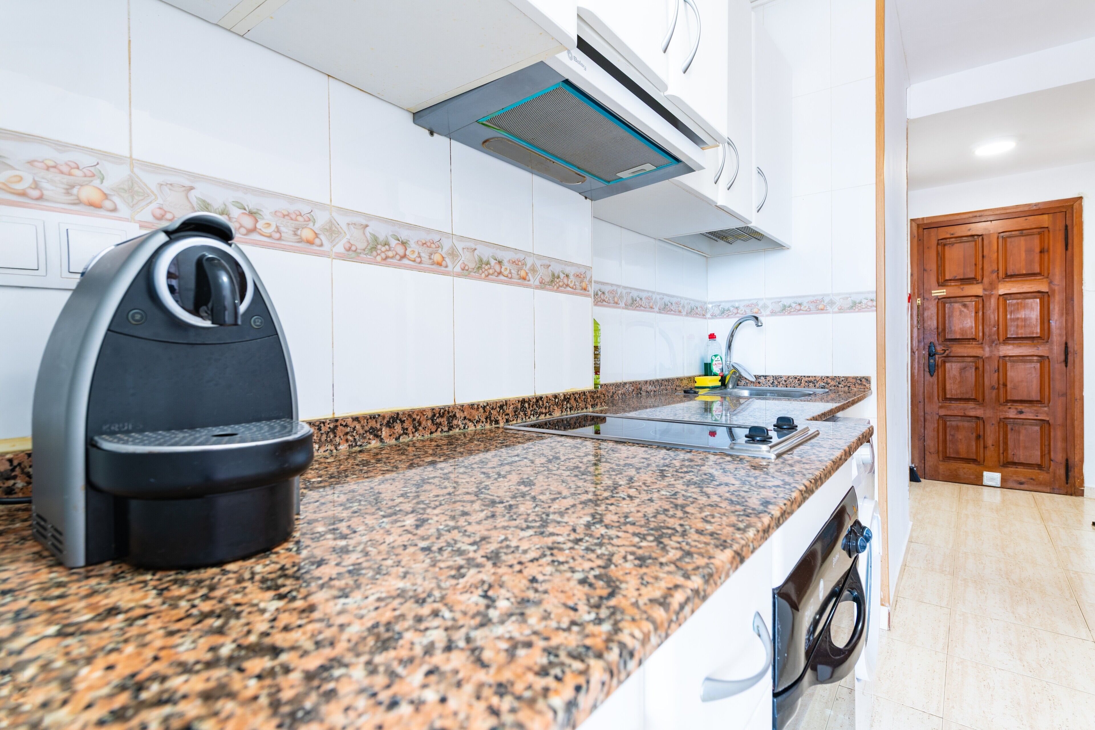 A kitchen with a coffee machine, a sink, and a washing machine.