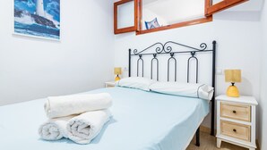 Un lit bien fait, avec du linge de lit blanc, une tête de lit et une table de chevet sur laquelle se trouve une lampe.