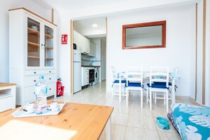 A room with a wooden table, a cabinet, a dining area with chairs, a kitchen in the background, and a fire extinguisher. - Apartment 'Los Arcos' with Shared Pool, Wi-Fi and Air Conditioning (Alcocéber)