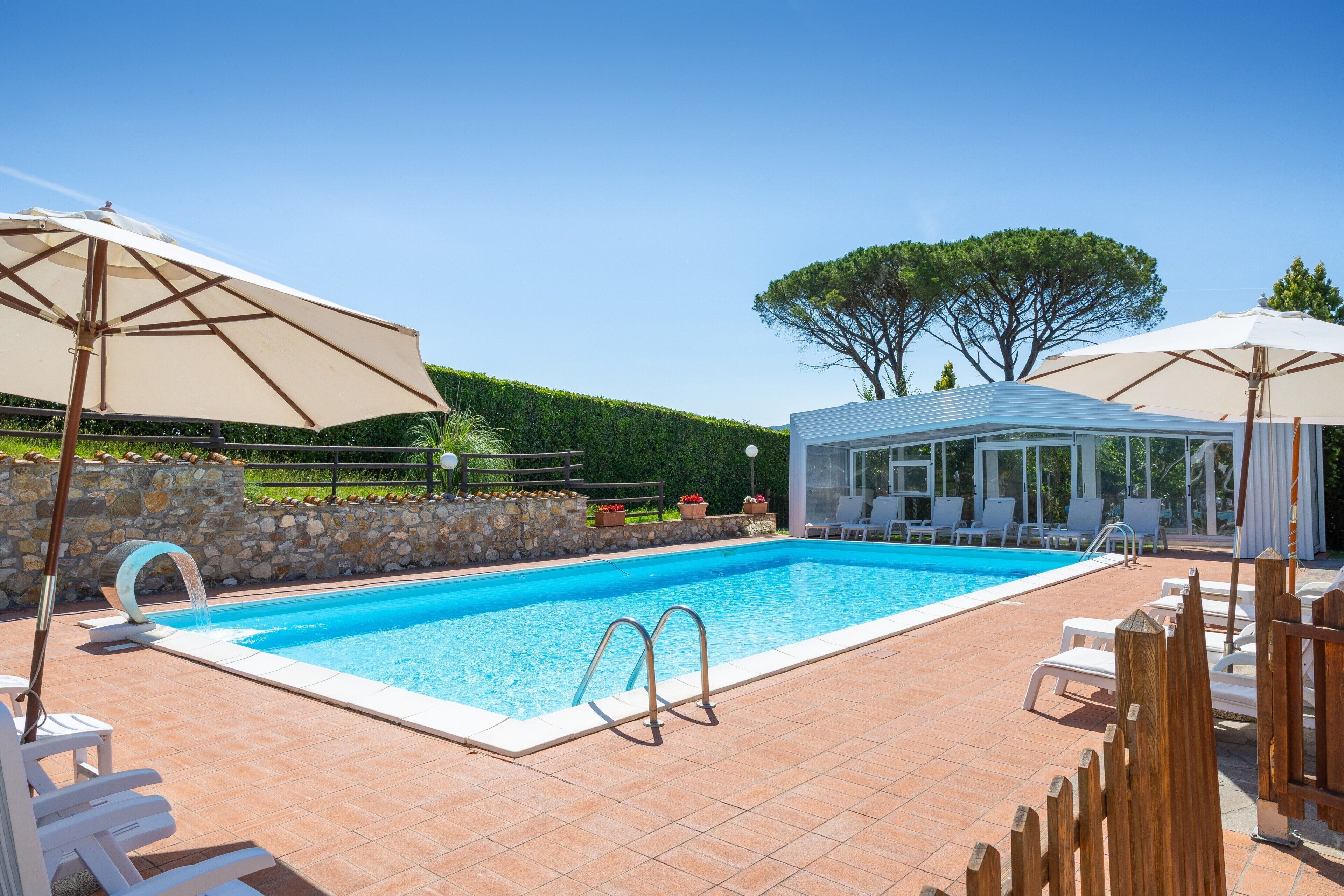 Une piscine à l’eau d’un bleu cristallin, entourée de chaises longues et de parasols, ainsi qu’un espace de détente abrité.