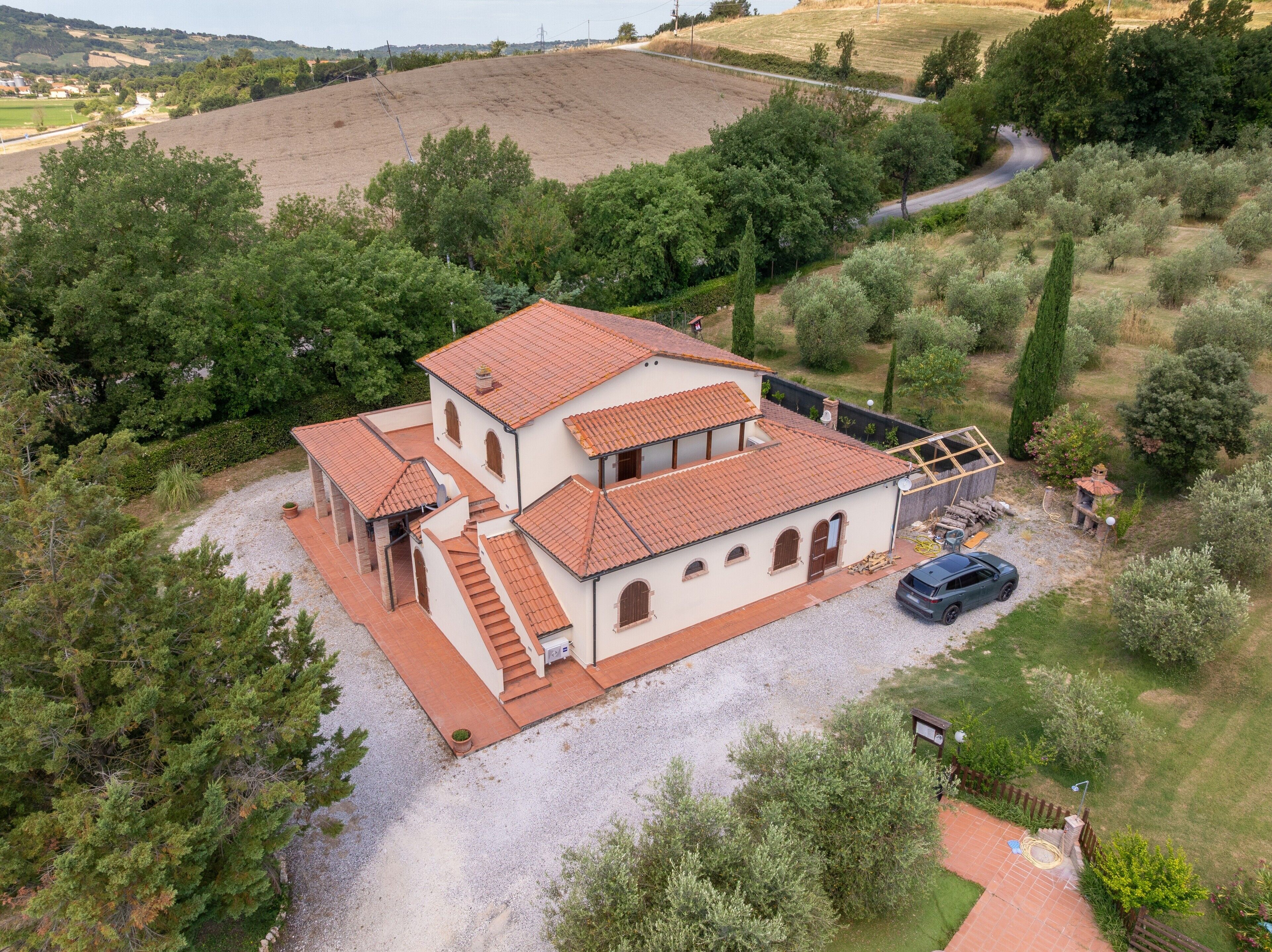 A two-story house with a tiled roof, a gravel driveway, and a car parked in the front.