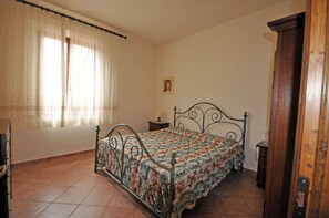 Un dormitorio con cama, mesita de noche, armario de madera, ventana con cortinas e imagen colgada en la pared.