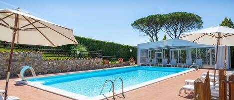 A swimming pool with a clear blue water, surrounded by lounge chairs and umbrellas, and a covered seating area.