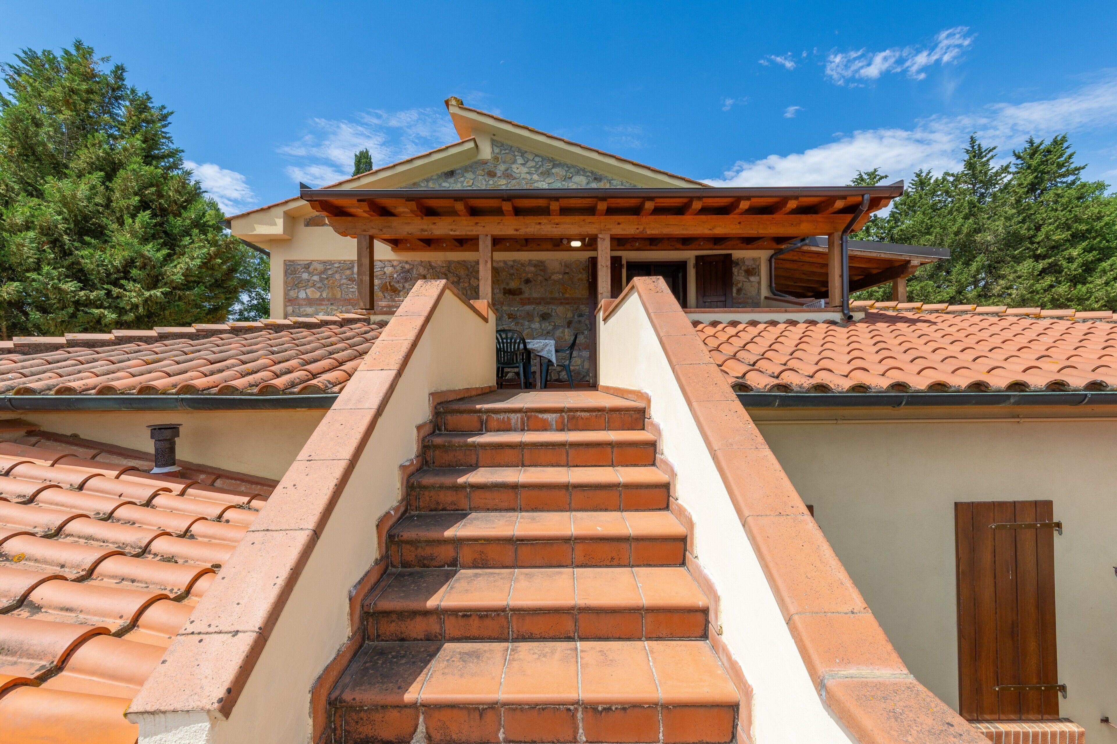 A staircase leading to a covered outdoor area with a stone wall and tiled roof.