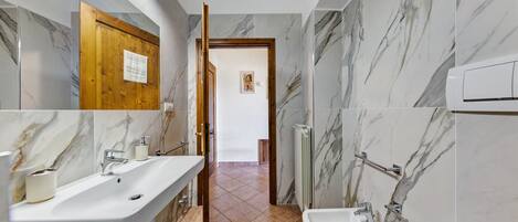 A bathroom with marble walls, a wooden door, and a white sink with a mirror.