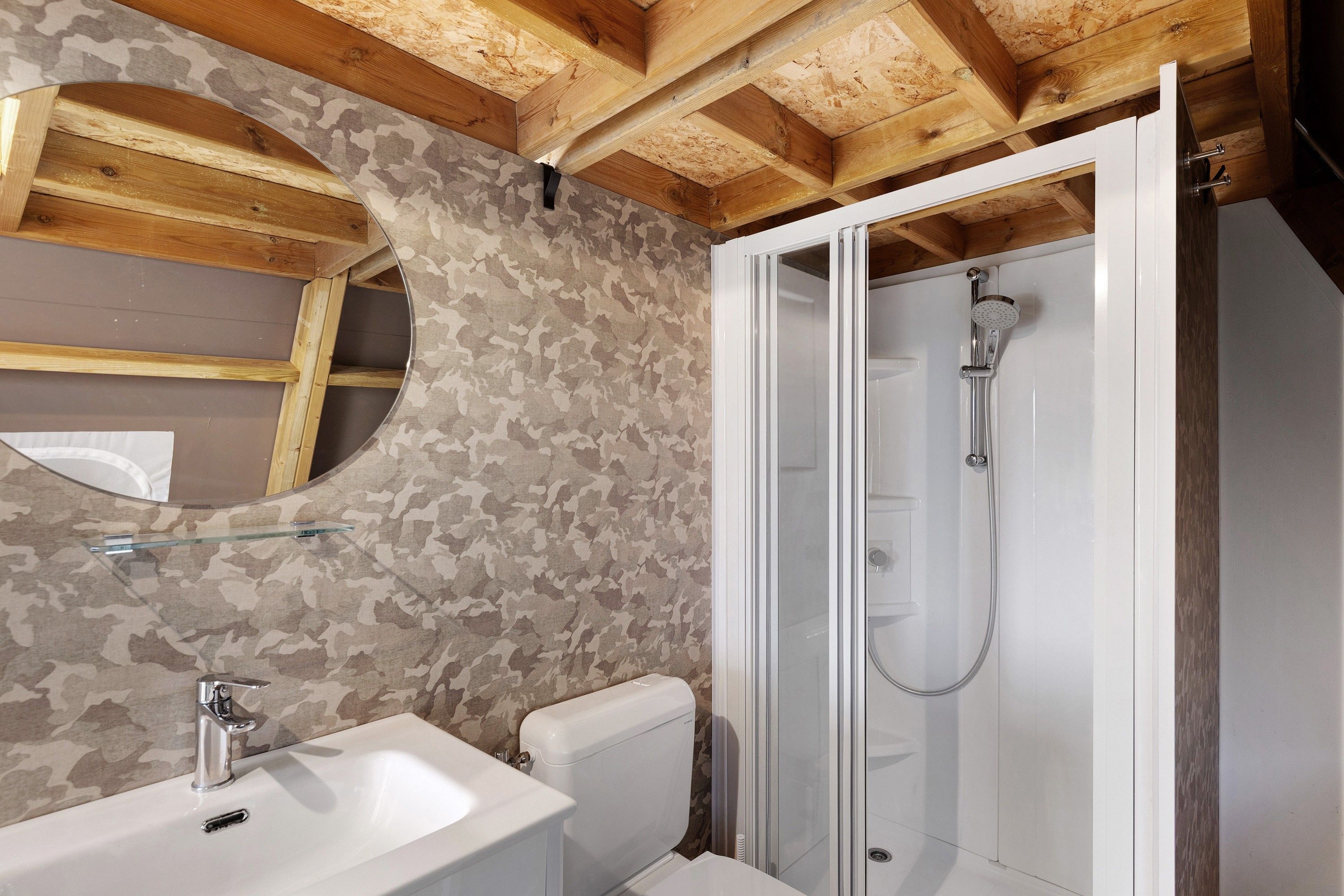 A bathroom with a wooden ceiling, a sink, a toilet, and a glass-enclosed shower.