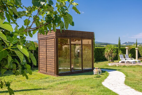 A wooden cabin with large glass windows, a stone pathway, and a garden with chairs and plants.