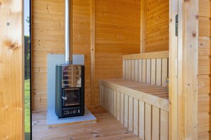 Una sauna con interior de madera, un banco y un calentador.