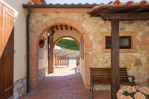 A stone archway leading to a pool area, wooden benches, and a hanging flower basket.