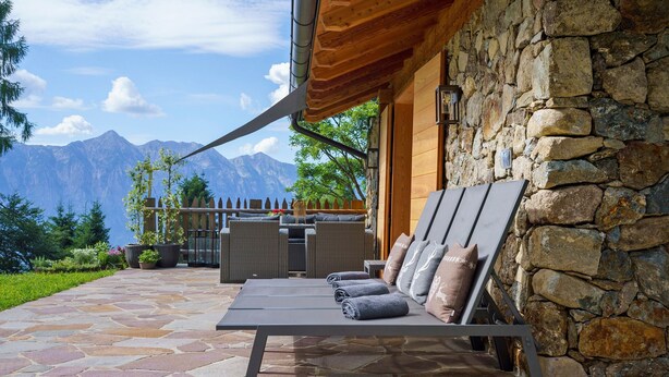 Un patio de piedra con una silla de descanso y cojines, un muro de piedra y vistas a la montaña.