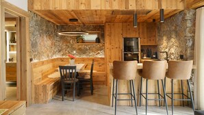 Un interior de madera con una pared de piedra, un comedor con sillas y una cocina con barra.