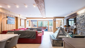 A modern interior with a dining area, red sofas, stone fireplace, and large windows.