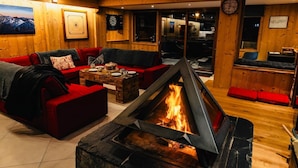 A cozy room with a fireplace, red sofas, a wooden coffee table, and a view through a glass door.