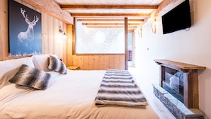 A wooden cabin room with a bed, a mounted television, and a fireplace.