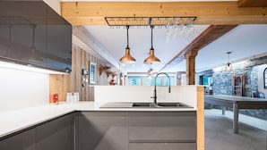 A modern kitchen with a central island, pendant lighting, and a stone wall in the background.