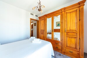 A bedroom with a large wooden wardrobe, a bed with white linens, and a chandelier. - Villa 'Cruz' with Private Terrace, Balcony and Air Conditioning (Fernán Pérez)