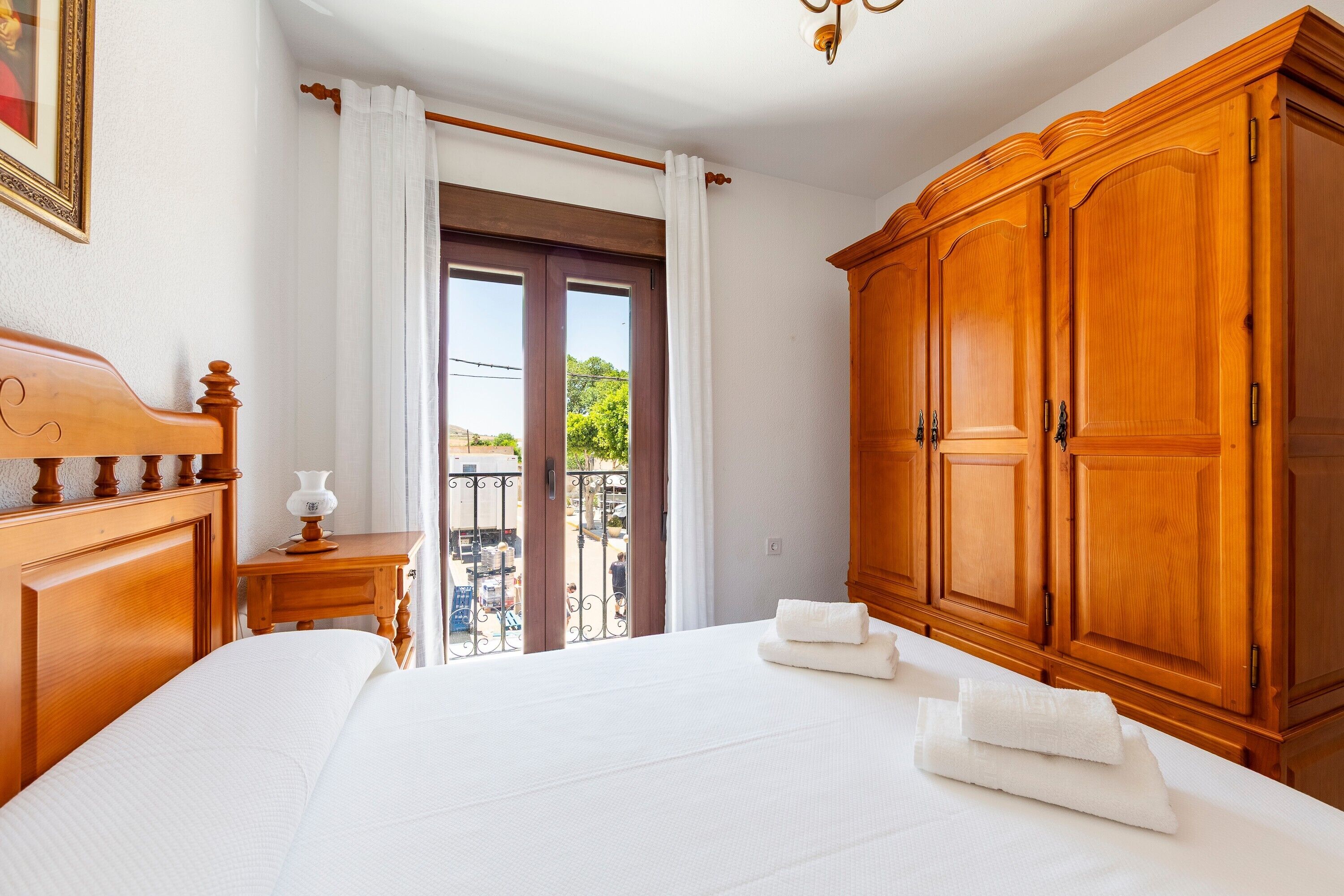 Habitación de hotel con una cama grande, un armario de madera, una mesita de noche con lámpara y vistas al exterior.
