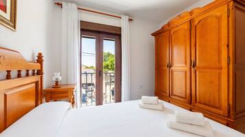 Habitación de hotel con una cama grande, un armario de madera, una mesita de noche con lámpara y vistas al exterior.