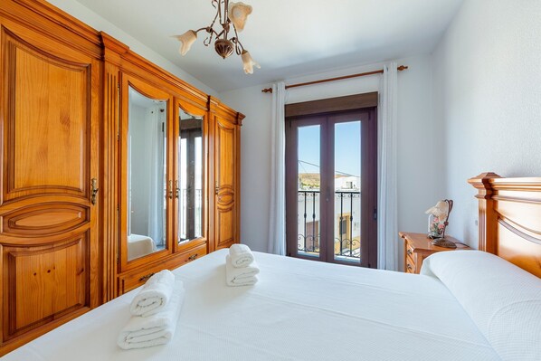 Habitación de hotel con una cama grande, armario de madera, un espejo, mesita de noche con lámpara y vistas al exterior.