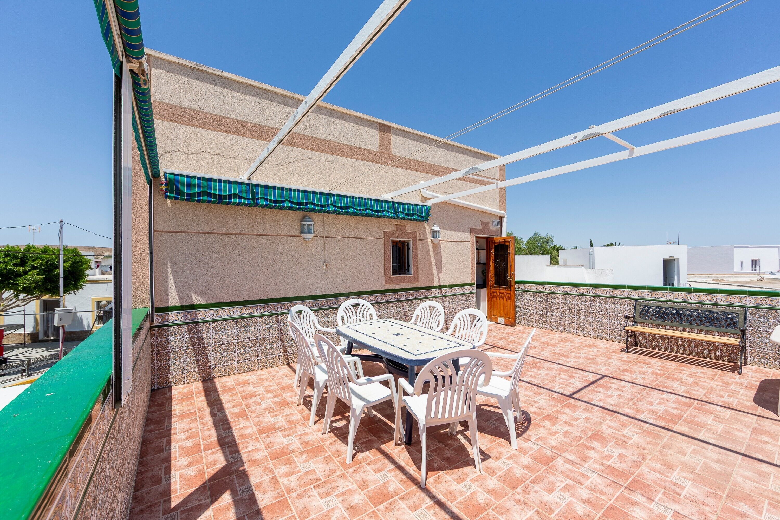 A patio with a table and chairs, a tiled floor, and a building with a green awning.
