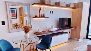 A modern living room with a glass coffee table, two blue chairs, a TV, and a wooden cabinet. - Brand New Studio in 4th Floor with Balcony (Playa del Carmen)