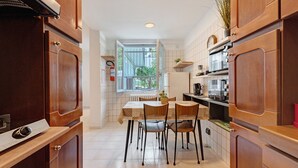 A kitchen with wooden cabinets, a dining table with chairs, a window with a view of greenery, and a built-in oven.