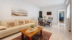 A living room with a sofa, coffee table, dining table, chairs, and artwork on the walls.