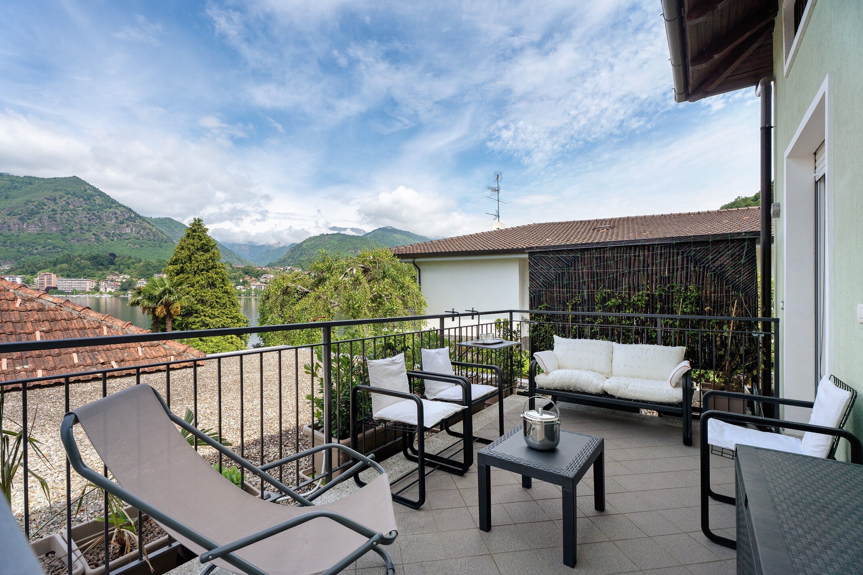 Ein Balkon mit Gartenmöbeln, Blick auf Berge und ein Gewässer im Hintergrund.