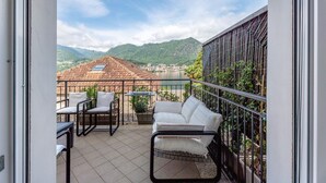 Ein Balkon mit einer weißen Couch, zwei Stühlen, einem kleinen Tisch und Blick auf Berge und Stadt.