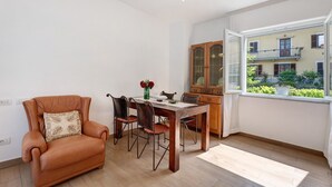 Ein Essbereich mit Tisch, Stühlen, einem Ledersessel, einem Schrank und einem Fenster mit Blick auf ein Gebäude und Grünflächen.