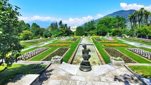 Ein formaler Garten mit symmetrischen Blumenbeeten, einer zentralen Fontäne und einem Berg im Hintergrund.