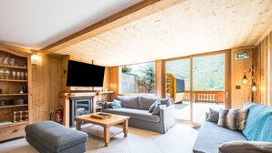 A wooden interior with a sofa, ottoman, and TV, a fireplace, and a view of the outdoors.