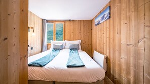 A wooden-paneled room with a bed, a window with a view, and a painting on the wall.