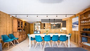 A modern kitchen with wooden walls, a dining table with blue chairs, and a bar area.