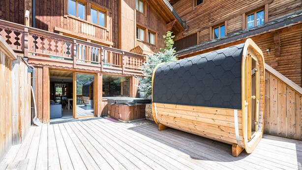A wooden cabin with a deck, a hot tub, and a covered outdoor seating area.