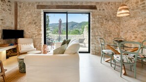 A stone-walled room with a sofa, chairs, a TV, and a view of mountains.