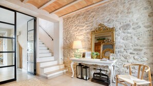 A room with a stone wall, a white staircase, a mirror, a lamp, and a chair.