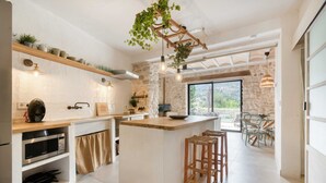 A modern kitchen with a central island, wooden bar stools, and a stone wall.