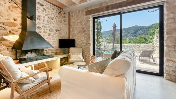 A stone-walled room with a fireplace, a TV, a sofa, and a view of the outdoors.
