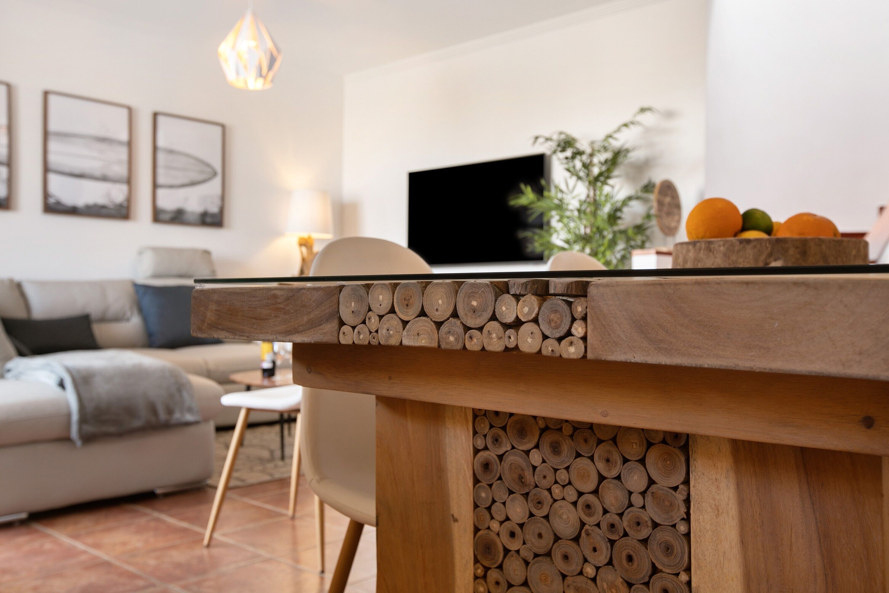 A modern living room with a wooden coffee table, a flat-screen TV, a sofa, and a dining area with a fruit bowl.