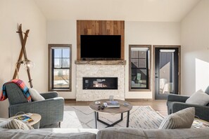 Una sala de estar con chimenea, dos sofás, una mesa de centro y un televisor sobre la chimenea.