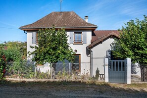 Ein zweistöckiges Haus mit grauer Tür, einer kleinen angebauten Garage und einem eingezäunten Garten.