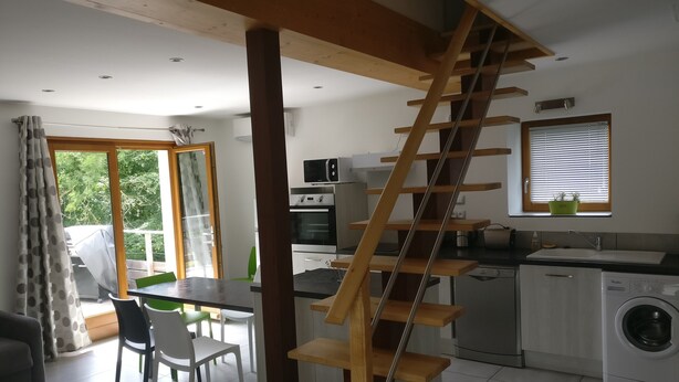 A modern kitchen with a wooden staircase, a dining area with chairs, and a washing machine.