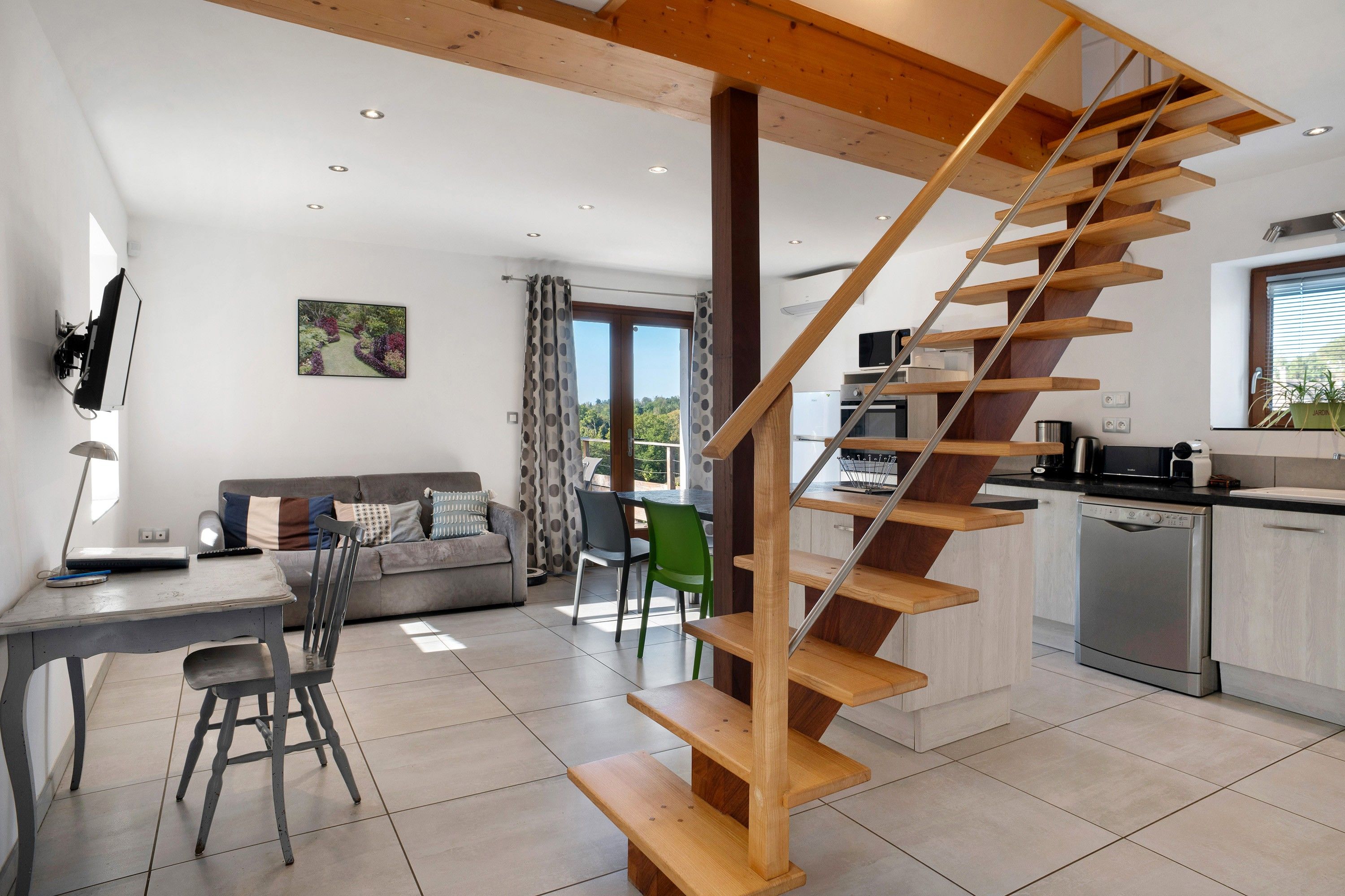 Una cocina moderna con una escalera de madera, un comedor con mesa y sillas, y una sala de estar con sofá y televisor.