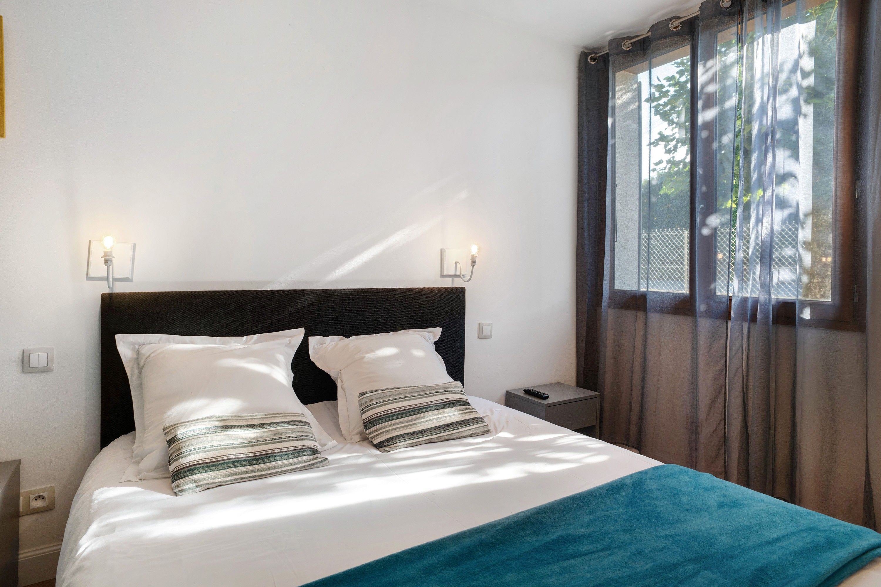 Une chambre d’hôtel avec un lit, deux lampes de chevet, une table de chevet, une télécommande et une fenêtre avec des rideaux.