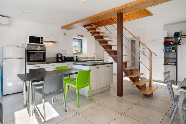 Una cocina moderna con una isla central, un área de comedor con sillas y una escalera de madera.