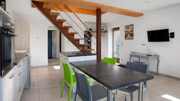 Una cocina moderna con estufa integrada, un área de comedor con mesa oscura y sillas verdes, y una escalera de madera.